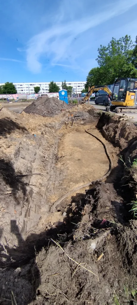 Ułożony kabel energetyczny na dnie wykopu przed zasypaniem, w tle koparka