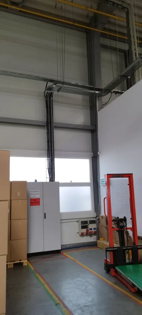 Rozdzielnica elektryczna w hali z kablami sprowadzonymi z korytka pod stropem